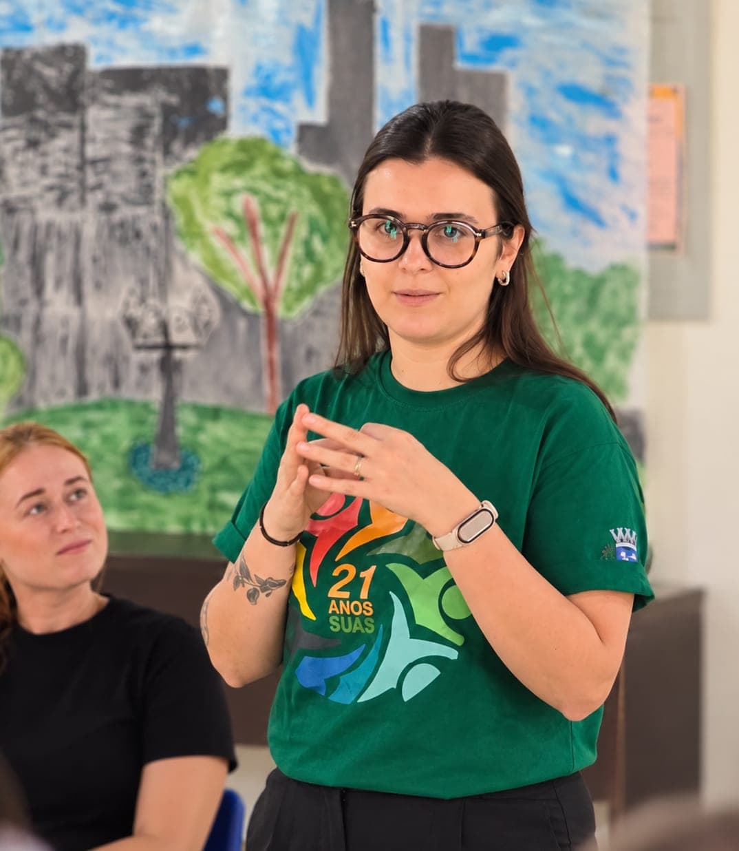Fernanda conversando com um grupo, vestindo a camiseta comemorativa dos 21 anos do SUAS